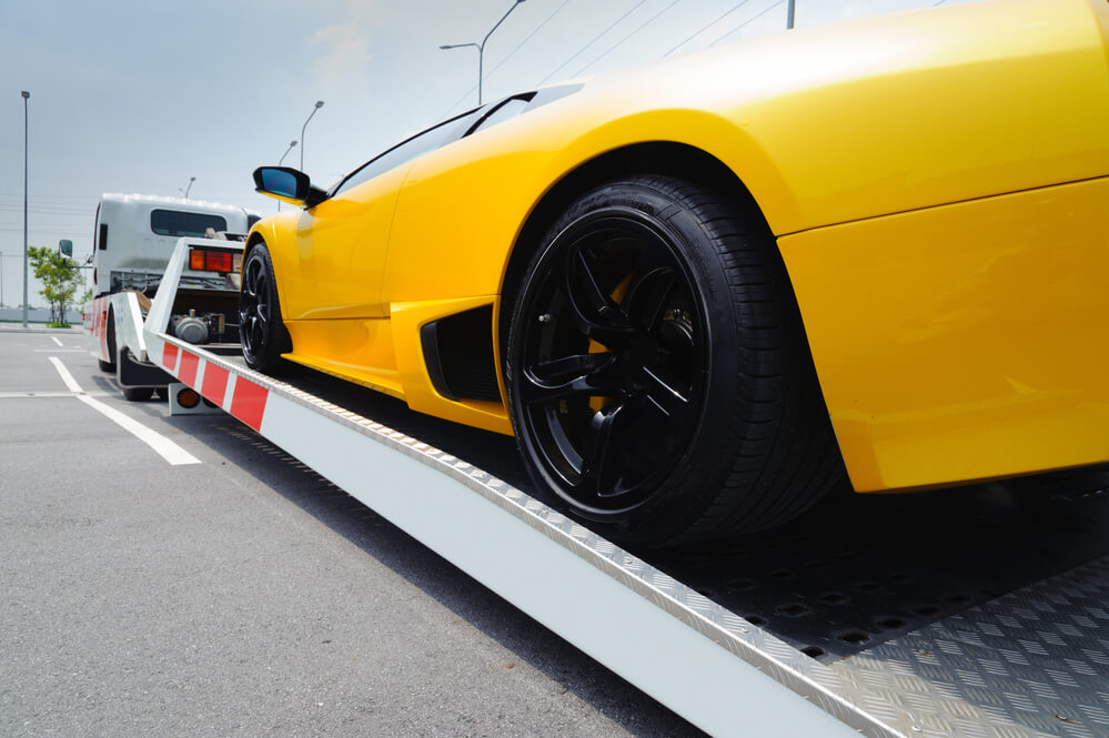 a rear angle of a yellow sports car being loaded onto a flat bed truck at tow truck Ipswich